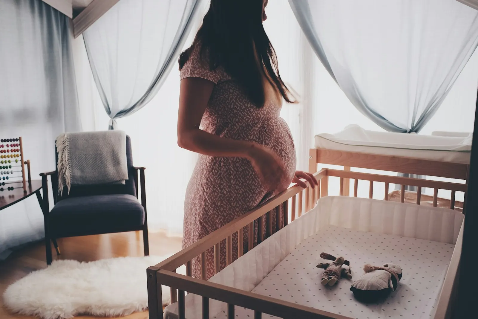 Een zwangere vrouw bij een wiegje in een zonnige babykamer