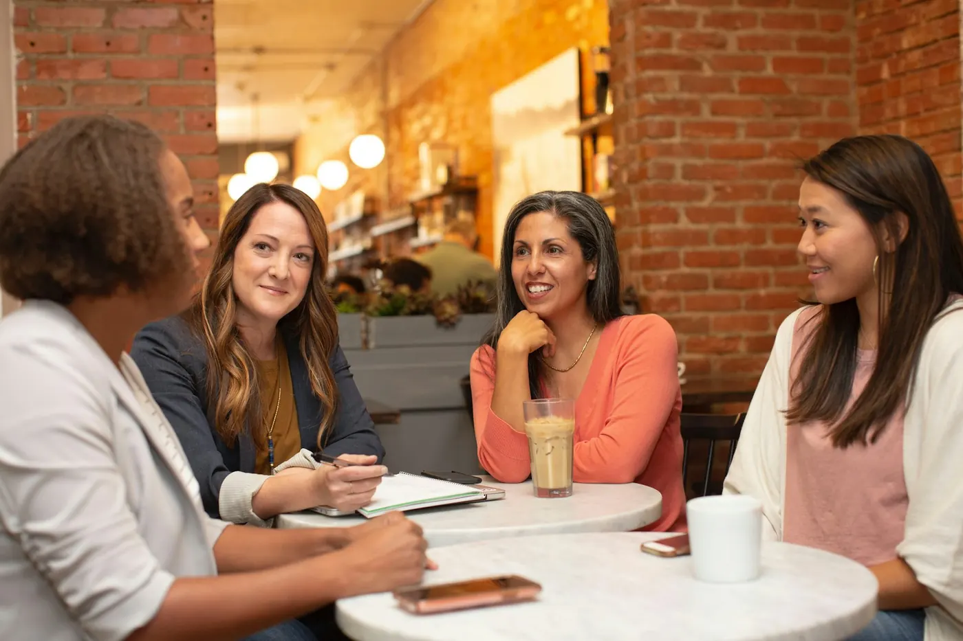 Four colleagues talking informally around a round table with coffee and a notebook