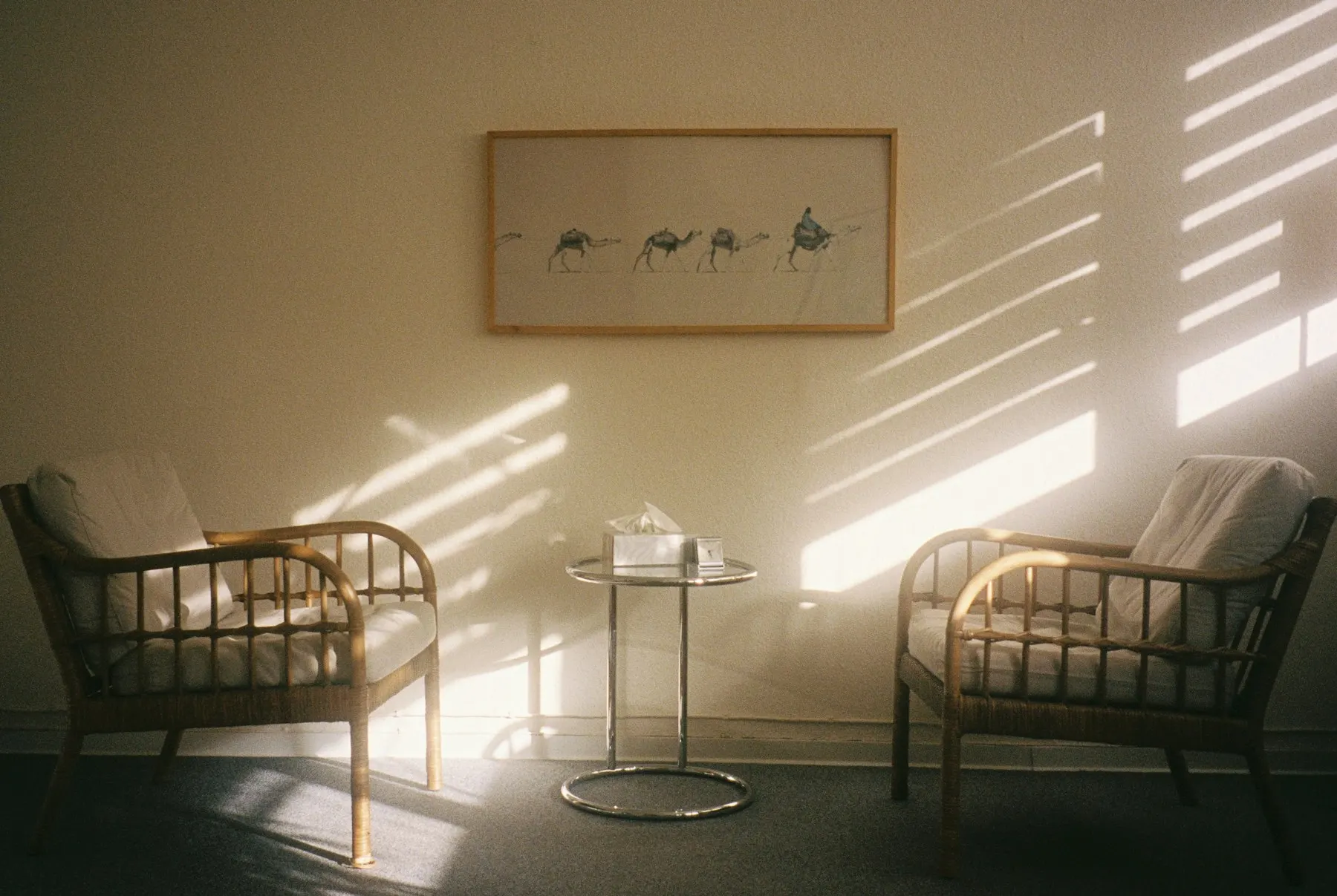 Two rattan armchairs facing each other in a quiet room with soft sunlight on the wall